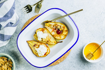Sweet baked pears with honey, nuts, cranberries and cinnamon in enameled baking bowl on stone background. Top view. Flat lay