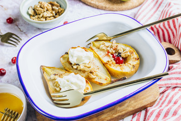Sweet baked pears with honey, nuts, cranberries and cinnamon in enameled baking bowl on stone background. Top view. Flat lay