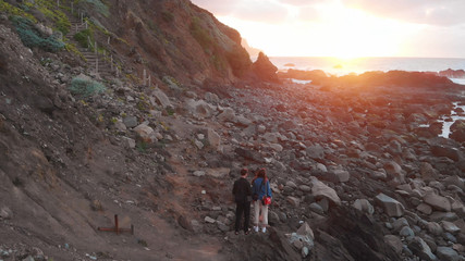 The guy and the girl stand on the ocean at sunset, at the foot of the cliffs, Benijo Beach, Tenerife, Canary Islands, Spain