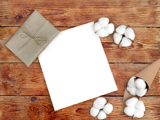 Fototapeta na wymiar Empty paper blank, gift box and cotton flowers on wooden background. Winter cozy minimalist concept of checklist for holiday with copy space. Top view.