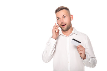 shocked businessman talking on smartphone and holding credit card isolated on white
