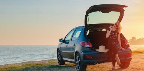 Young woman sits in a car trunk by the sea on the beach. Summer, sunset, road traveling concept. Copy space. © 22Imagesstudio