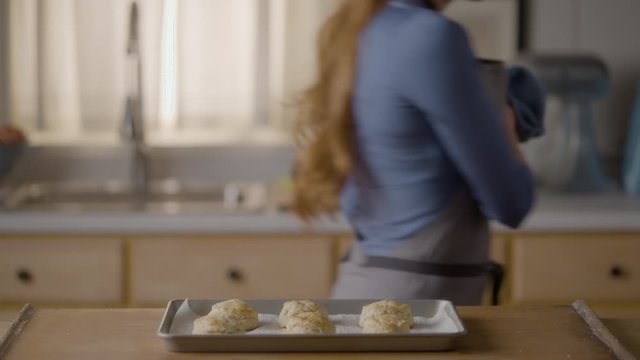 Woman places a pan of freshly baked biscuits on a wooden countertop, with sound