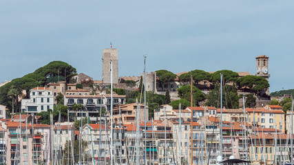 Distant view on the Cannes castle preceded by the masts of yachts moored in the marina.