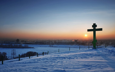 Panorama urban winter view evening sunset. Big christian cross on a mountain above the city