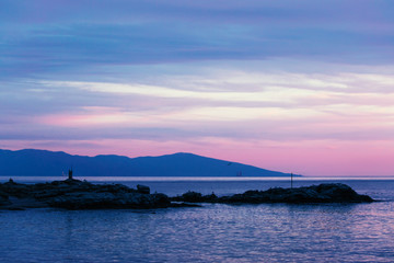 Rocky island silhouette in the sea during purple sunset.