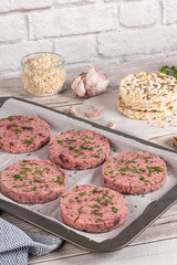 Raw veggie burger with beetroot and white beans with parsley leaves on wood cutting board.