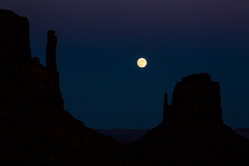 Full moon in dark sky above silhouette of desert towers in Souther Utah/Arizona Monument Valley.