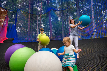 Young mother and her two children playing with big gym colorful balls in outdoor net amusement park