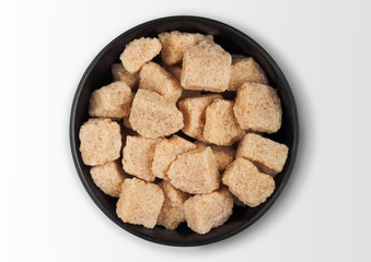 Black bowl plate of natural brown unrefined sugar cubes on white background.