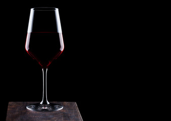 Glass of red wine on wooden board on black background. Space for text