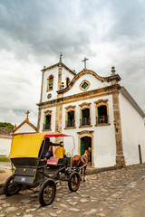 Fototapeta na wymiar Horse and carriage on the cobblestone street in the historic church in Paraty, Rio de Janeiro, Brazil. UNESCO World Heritage Site on the Brazilian Coast