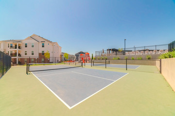 Fototapeta na wymiar Tennis court at a neighborhood with townhouses and playground in the background