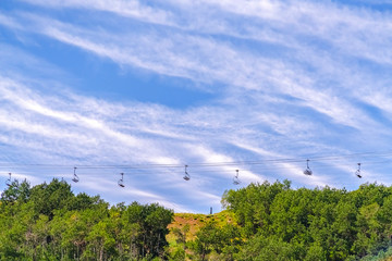 Lush green trees andski resort chairlifts against cloudy blue sky during summer