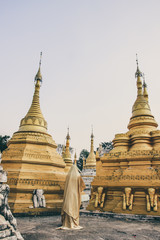 Creature in a gold floaty robe walking along ancient golden Myanmar Buddhist temples and stupas experimental shoot