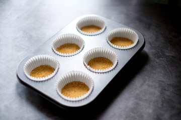 Obraz na płótnie Canvas Mini Cheesecakes Recipe. Biscuits mix with butter on 6 muffin liners in a muffin pan.