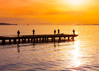 Fototapeta premium fishermanes silhouette fishing at sunset on the see