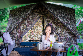 little asian girl sitting and eating breakfast in front of tent while going to camping.The concept of outdoor activities and adventures in nature