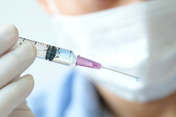 doctor's hand holds a syringe and a blue vaccine bottle at the hospital. Health and medical concepts