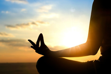 Silhouette of a woman doing meditation on the beach of the sea during the morning hours.