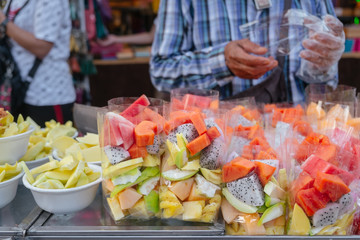 Various fresh tropical fruits in plastic bags and foam bowls for sale at fruit stall in local street food market. Bangkok, Thailand.