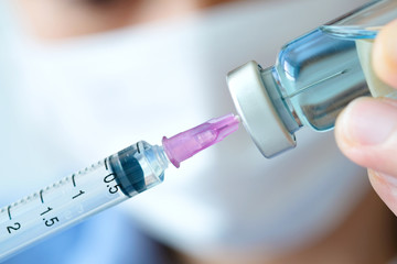 doctor's hand holds a syringe and a blue vaccine bottle at the hospital. Health and medical concepts