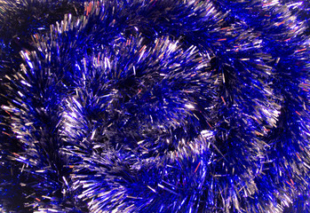New Year background photo with glowing blue tinsel. Close-up of shiny metallic texture of holiday decoration.