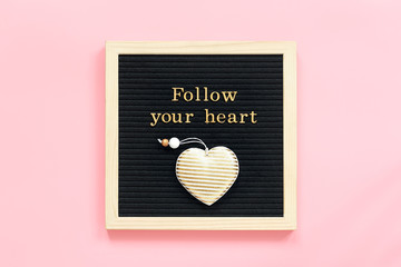 Follow your heart. Motivational quote in gold letters and decorative textile heart on black letter board on pink background. Top view Flat lay Concept inspirational quote of the day