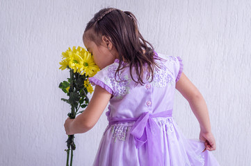 Little girl from back, in stylized pose, smells closer, bouquet of flowers in her left hand