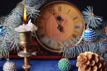Table clock, burning candle, spruce branch and Christmas decorations on a table with a blue tablecloth