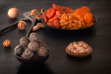 Natural healthy raw energy bites and mix of dried fruits with nuts on a black table. Low key.