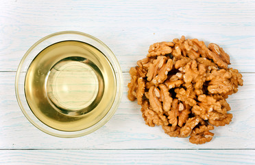 Pile walnuts heap and walnuts oil in glass bowl on a white wooden background. Top view.