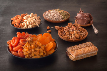 Mix of dried fruits, energy bites, chocolate paste and nuts on a black table. Close-up.