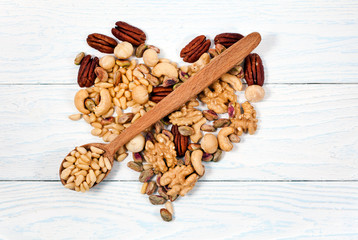 Heart made of different nuts with spoon on wooden background. Pecan, macadamia, pistachio, cashew, walnuts.