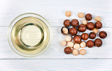 Macadamia nuts heap and macadamia oil in glass bowl on a white wooden background. Top view.