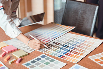 Creative young graphic designer choosing a color from the sampler and drawing on a digital tablet computer at workplace.