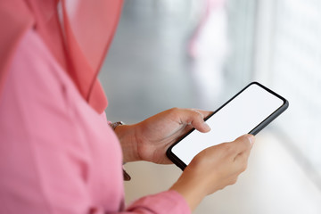 Cropped shot of muslim business woman in pink hijab and casual wear standing and using mockup smartphone. White screen mockup mobile phone for graphic montage.