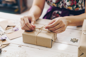 Close up of hands holding wrapping gift box on wooden table with xmas decoration.