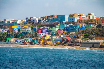 Colorful houses line the hill side overlooking the beach in San Juan, Puerto Rico. - obrazy, fototapety, plakaty