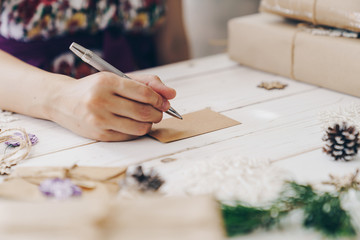 Close up of hands woman writing empty wishlist and christmas card on wooden table with xmas decoration.