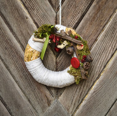 Decorated handmade Christmas wreath hanging on the rope on the rustic wooden door