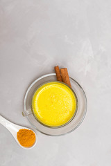 Obraz na płótnie Canvas Cup of golden turmeric milk with cinnamon sticks and turmeric powder on grey concrete table