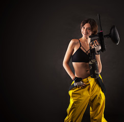 pretty woman in equipment with a paintball gun on a black background. Leisure
