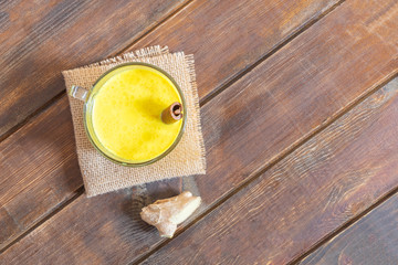 Golden Turmeric Milk in a glass cup with cinnamon and ginger on wooden table.