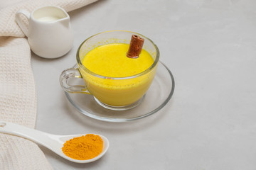 Golden Turmeric Milk with turmeric powder, cinnamon stick and milk on grey neutral table