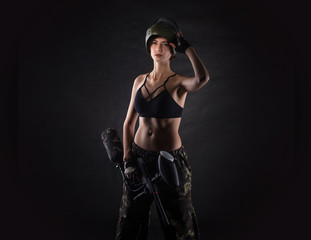 Fototapeta na wymiar pretty woman in equipment with a paintball gun on a black background. Leisure