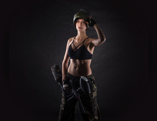 pretty woman in equipment with a paintball gun on a black background. Leisure