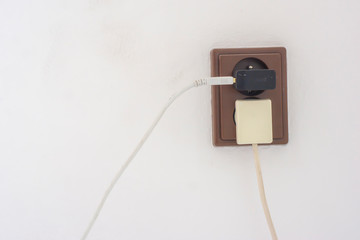 A simple socket with plugged charging plugs from the phone and a lamp on a white wall