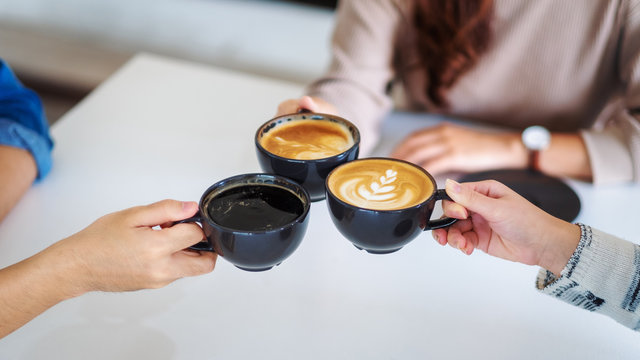 Closeup image of people enjoyed drinking and clinking coffee cups together on the table in cafe