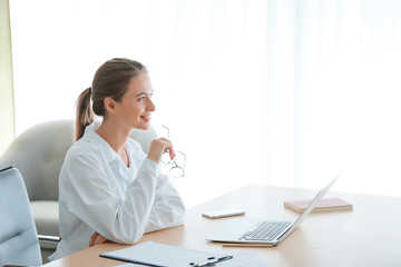 Female doctor with laptop sitting at table in clinic